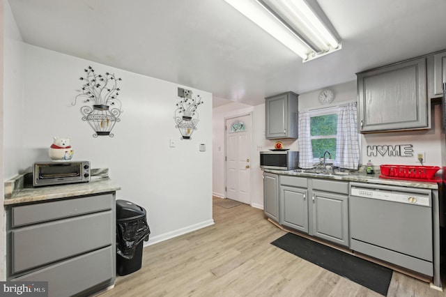 kitchen with dishwasher, stainless steel microwave, gray cabinets, a sink, and light wood finished floors
