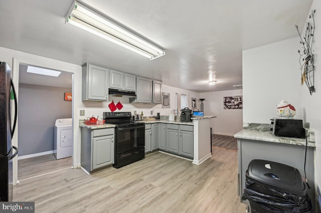 kitchen featuring black appliances, gray cabinetry, washer / dryer, under cabinet range hood, and a peninsula