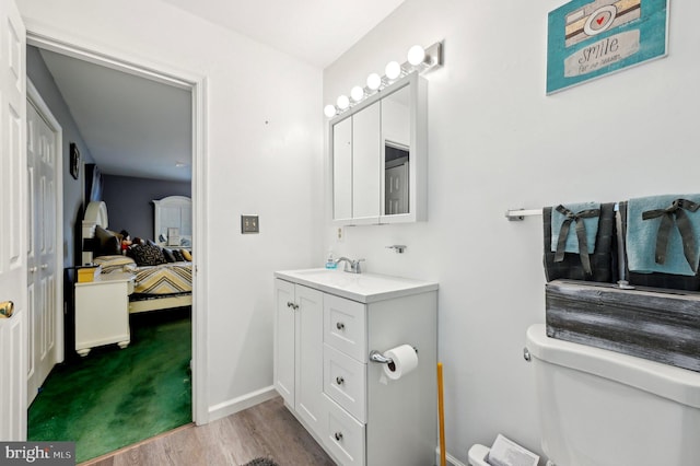 ensuite bathroom featuring wood finished floors, vanity, toilet, and baseboards