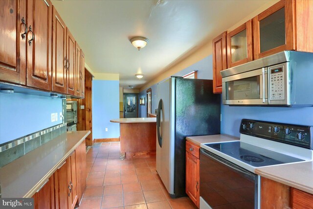 7395 Jonestown Rd, Harrisburg, PA 17112 - kitchen with glass insert cabinets, light countertops, brown cabinets, light tile patterned floors, and stainless steel appliances