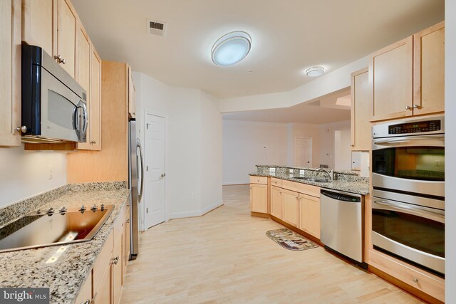 kitchen with a sink, light brown cabinetry, light wood-type flooring, stainless steel appliances, and light stone countertops