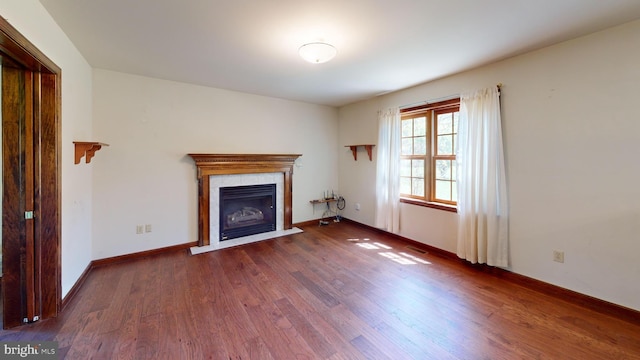unfurnished living room with a tiled fireplace, baseboards, wood finished floors, and visible vents