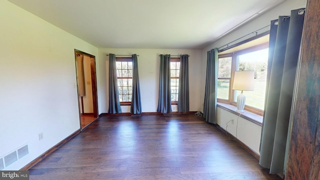 unfurnished room with visible vents, baseboards, and dark wood-style floors