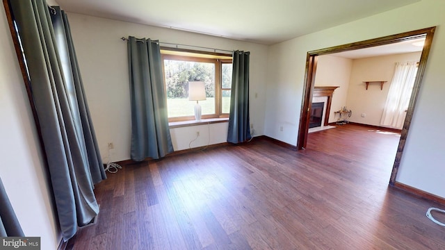 spare room featuring a fireplace with flush hearth, baseboards, and dark wood-style flooring