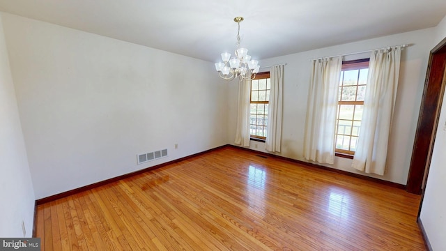 empty room featuring light wood-type flooring, baseboards, a notable chandelier, and visible vents
