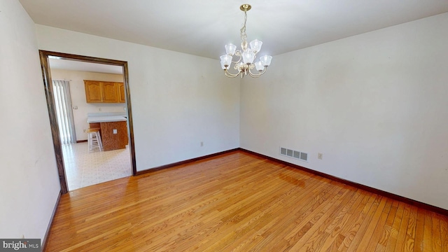 spare room with a chandelier, baseboards, visible vents, and light wood finished floors