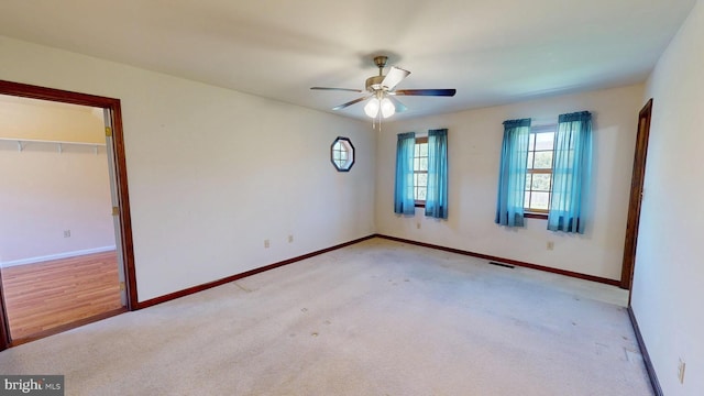 spare room with ceiling fan, light colored carpet, baseboards, and visible vents