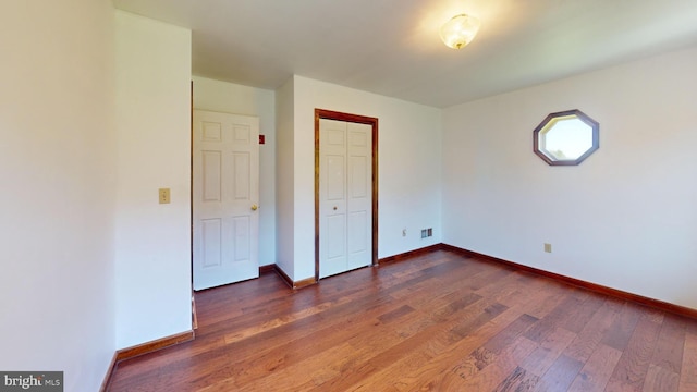 unfurnished bedroom with baseboards, dark wood-style flooring, visible vents, and a closet