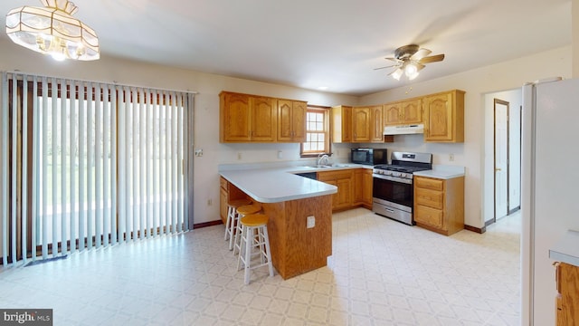 kitchen with a ceiling fan, stainless steel range with gas stovetop, a sink, a peninsula, and light floors