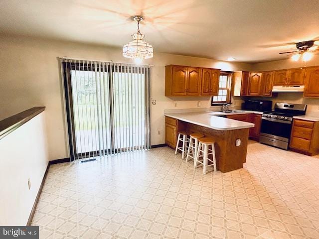 kitchen with under cabinet range hood, a peninsula, brown cabinets, and stainless steel stove