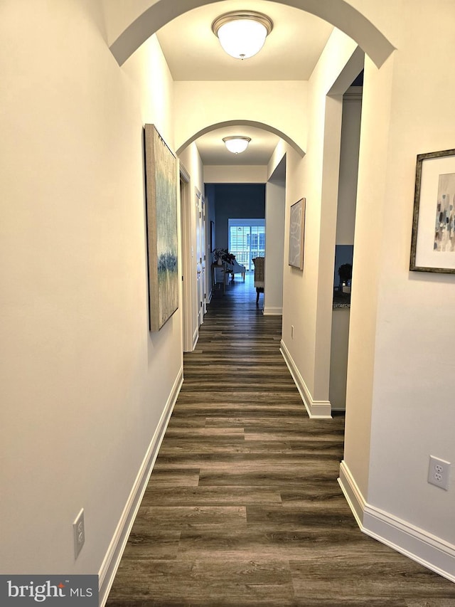 hallway with dark wood-style floors, baseboards, and arched walkways