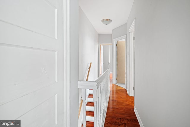 corridor featuring baseboards, wood finished floors, and an upstairs landing