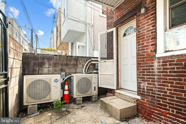 view of exterior entry with brick siding, ac unit, and fence