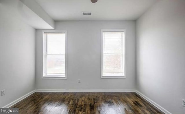 unfurnished room featuring baseboards, plenty of natural light, dark wood finished floors, and visible vents