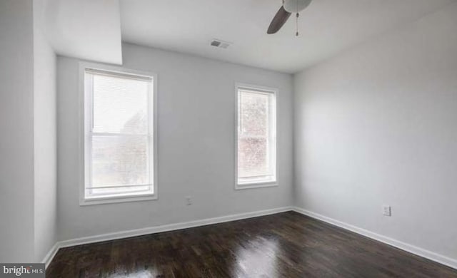 empty room with dark wood-style flooring, ceiling fan, visible vents, and baseboards