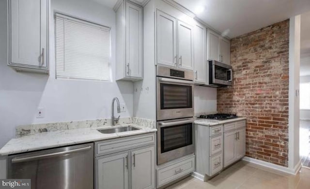 kitchen featuring appliances with stainless steel finishes, a sink, brick wall, gray cabinets, and baseboards