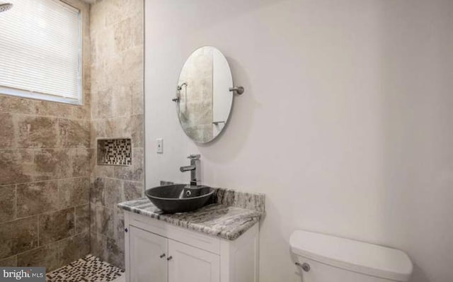 bathroom featuring toilet, tiled shower, and vanity