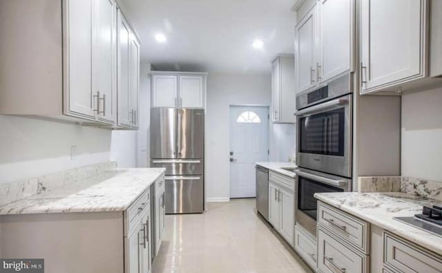 kitchen featuring baseboards, recessed lighting, light stone counters, light tile patterned floors, and stainless steel appliances