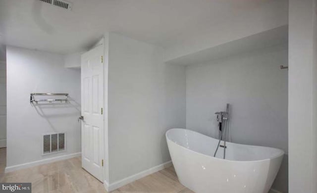 bathroom with a freestanding bath, baseboards, and visible vents