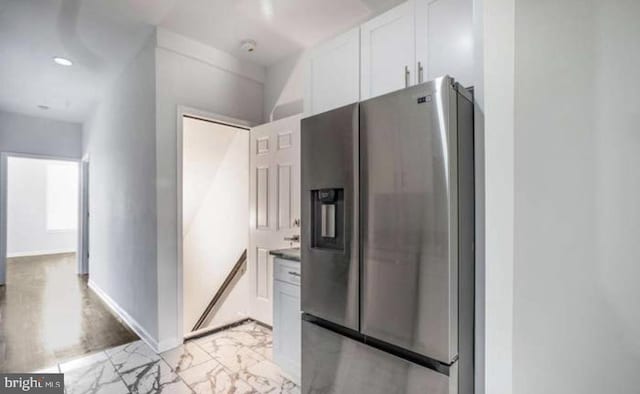 kitchen featuring dark countertops, stainless steel fridge with ice dispenser, baseboards, marble finish floor, and white cabinetry