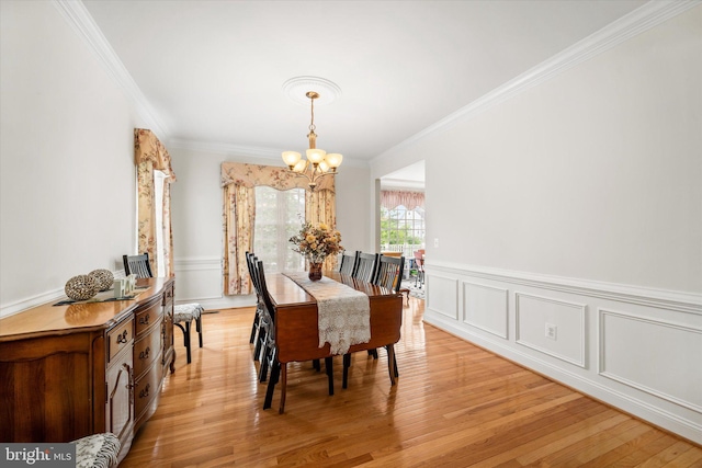 dining area with wainscoting, a chandelier, ornamental molding, and light wood finished floors