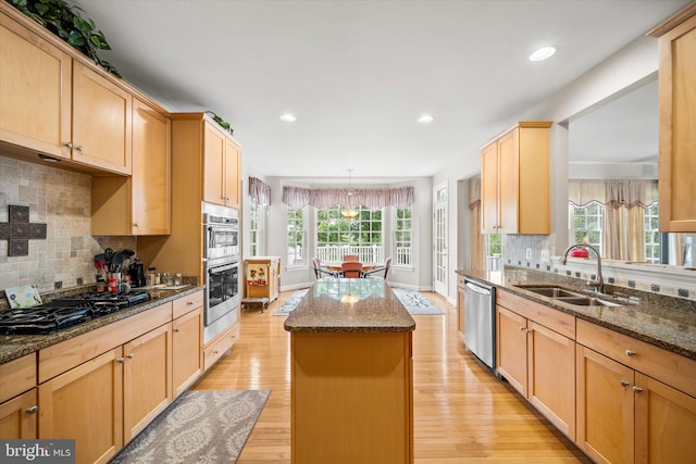 kitchen with decorative backsplash, a kitchen island, appliances with stainless steel finishes, a sink, and light wood-style flooring