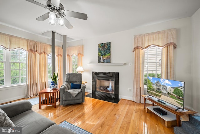 living area with baseboards, a fireplace with flush hearth, a ceiling fan, and hardwood / wood-style floors
