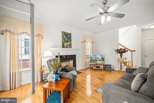 living room featuring stairway, a ceiling fan, a glass covered fireplace, and hardwood / wood-style floors
