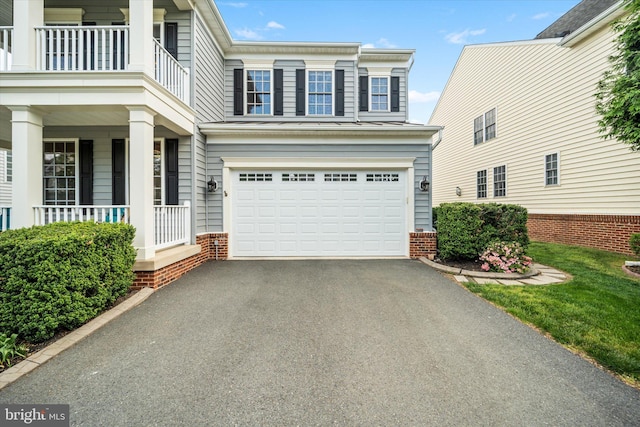 view of side of home with a porch, brick siding, an attached garage, and aphalt driveway