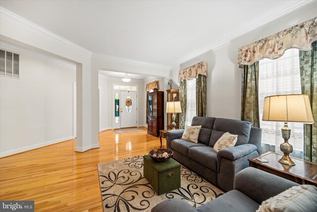 living area with baseboards, visible vents, ornamental molding, and light wood-type flooring