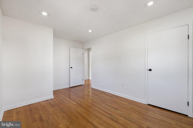 empty room with wood-type flooring, baseboards, and recessed lighting