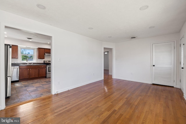 unfurnished living room featuring wood finished floors, visible vents, baseboards, and a sink