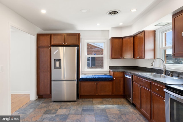 kitchen with dark countertops, a sink, stainless steel appliances, stone finish floor, and visible vents