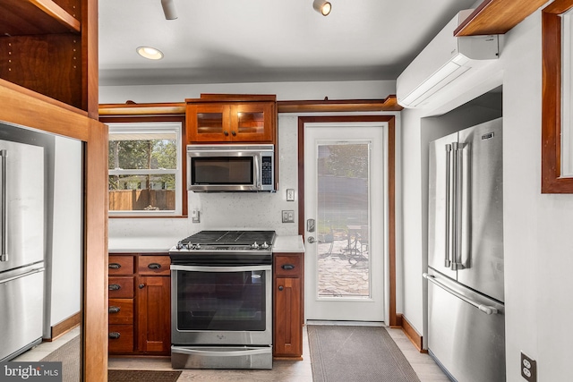 kitchen featuring glass insert cabinets, baseboards, light countertops, brown cabinets, and stainless steel appliances