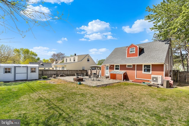 rear view of house featuring an outdoor structure, a fire pit, a fenced backyard, a shed, and a shingled roof