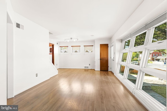 unfurnished living room with baseboards, visible vents, light wood-style flooring, and rail lighting