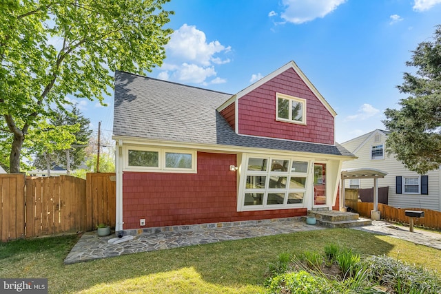 rear view of property featuring a lawn, roof with shingles, fence, and a patio