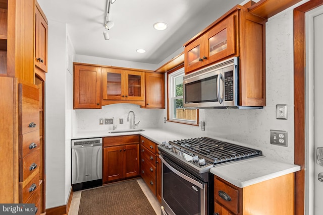 kitchen with light countertops, appliances with stainless steel finishes, brown cabinetry, and a sink
