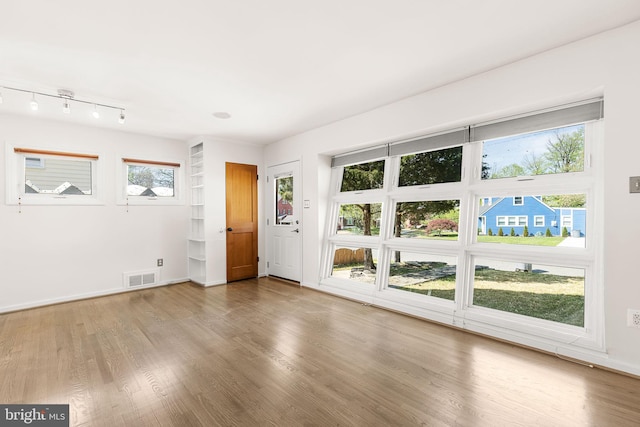 unfurnished room with baseboards, a wealth of natural light, wood finished floors, and visible vents