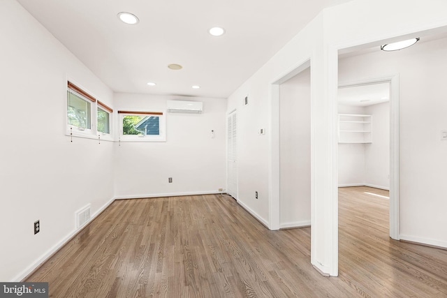 empty room with baseboards, a wall unit AC, wood finished floors, and visible vents