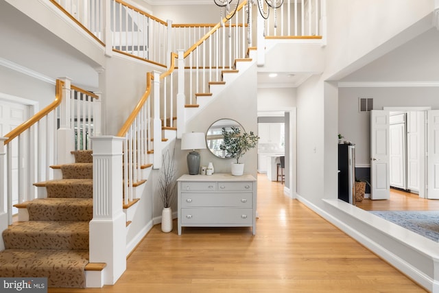 staircase with a high ceiling, wood finished floors, baseboards, and ornamental molding