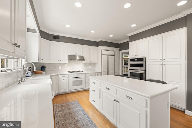 kitchen with a sink, stainless steel double oven, a center island, white cabinetry, and crown molding