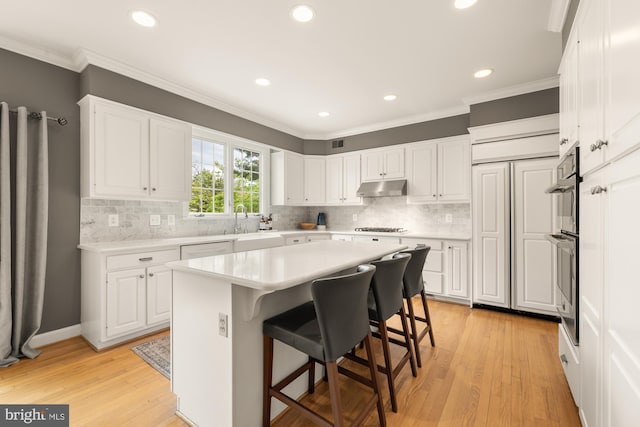 kitchen with under cabinet range hood, gas cooktop, white cabinets, light countertops, and ornamental molding
