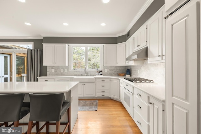 kitchen with a sink, gas stovetop, crown molding, under cabinet range hood, and light countertops