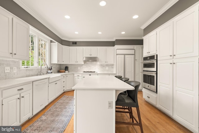 kitchen with dishwasher, a sink, stainless steel double oven, under cabinet range hood, and light wood-type flooring