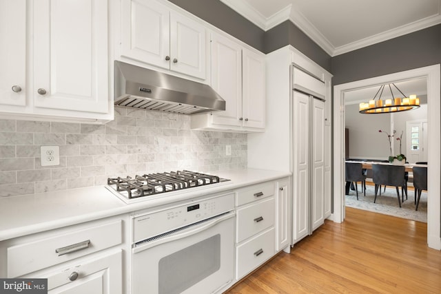 kitchen with white appliances, under cabinet range hood, a chandelier, ornamental molding, and white cabinetry