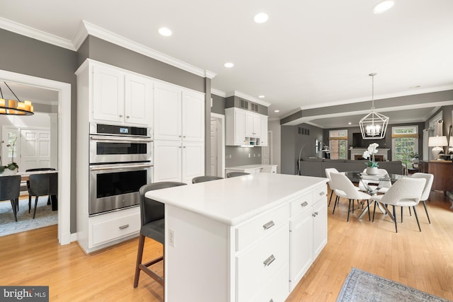 kitchen with a chandelier, stainless steel double oven, recessed lighting, white cabinets, and light wood-style floors