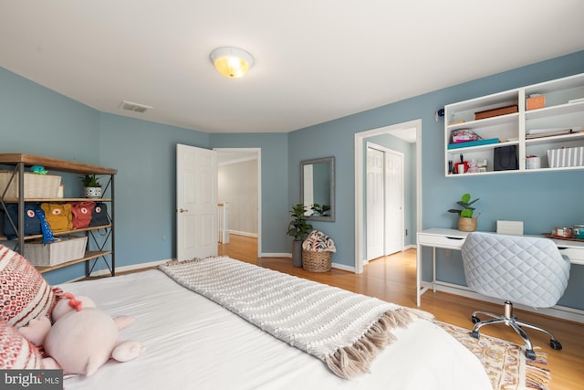bedroom with wood finished floors, a closet, an office area, and baseboards