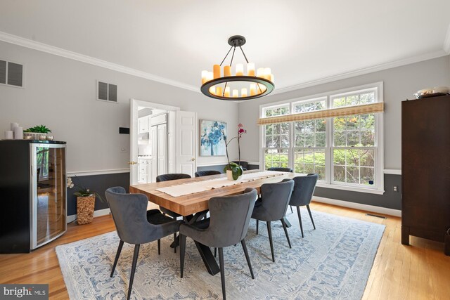 dining space featuring ornamental molding, wine cooler, a chandelier, light wood-style floors, and baseboards