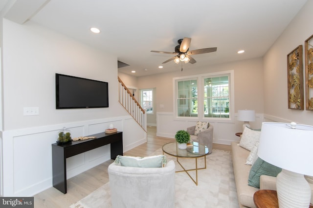 living area with light wood finished floors, recessed lighting, stairway, ceiling fan, and wainscoting